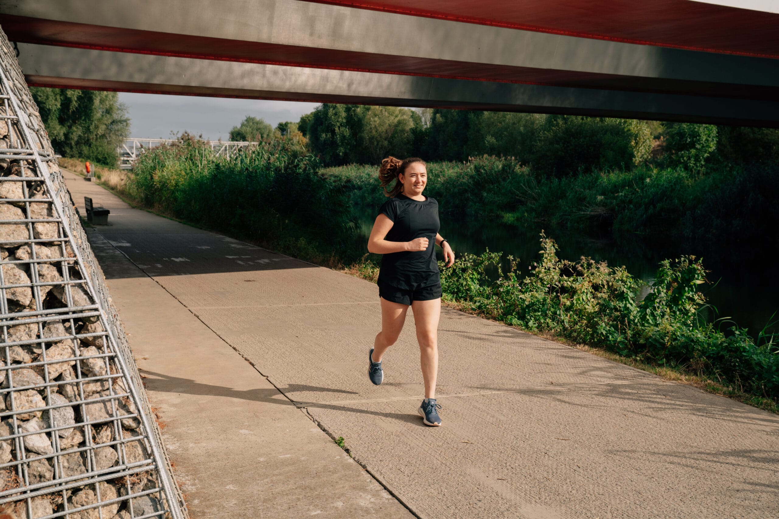 woman running under a bridge near a river