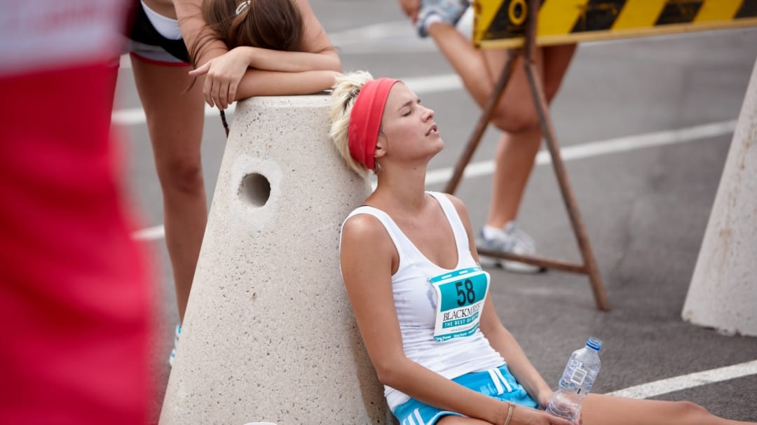 A women in a marathon sitting on the floor with a water bottle