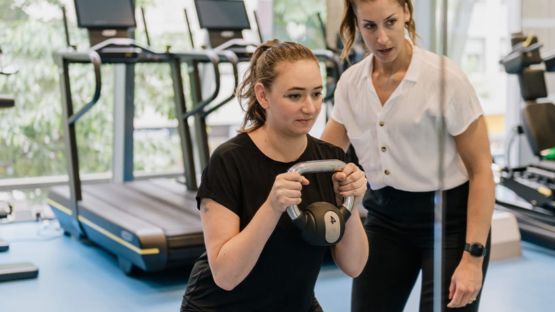 patient with kettle bell in recovery gym with clinician support