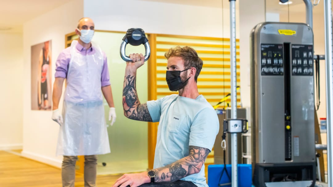 patient holding kettle bell up in the air with clinician watching in gym